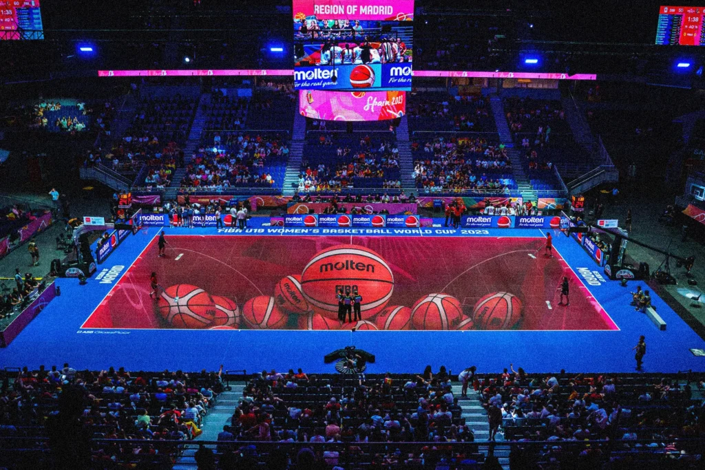 An indoor basketball court featuring ASB GlassFloor's illuminated LED flooring with dynamic lines, score displays, and motion tracking overlays.