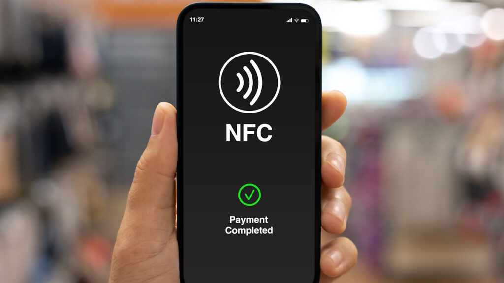 A smartphone hovering over a payment terminal with digital signals illustrating contactless interaction—representing the upgraded capabilities of NFC Release 15.