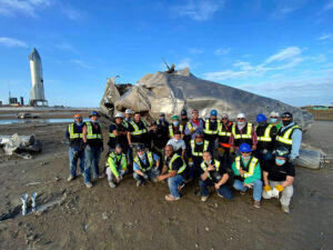 SpaceX workers assembling spacecraft at Starbase with safety gear, surrounded by high-tech launch infrastructure and towering rockets.